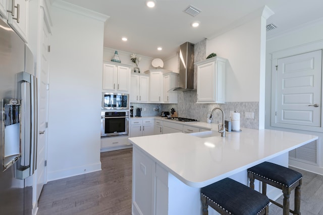 kitchen featuring wall chimney range hood, appliances with stainless steel finishes, a kitchen bar, sink, and dark wood-type flooring