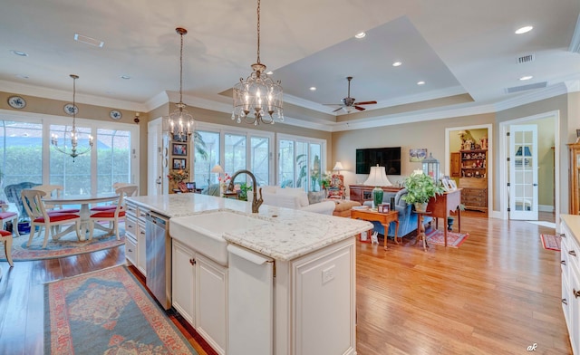 kitchen featuring stainless steel dishwasher, ornamental molding, a kitchen island with sink, decorative light fixtures, and light hardwood / wood-style flooring