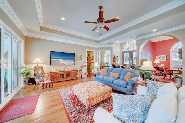 living room with ceiling fan, a raised ceiling, ornamental molding, and light hardwood / wood-style flooring