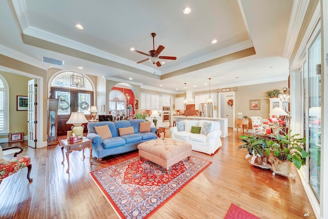 living room featuring a tray ceiling, crown molding, and light wood-type flooring