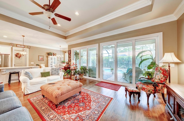 living room featuring hardwood / wood-style flooring, ceiling fan with notable chandelier, crown molding, and a tray ceiling