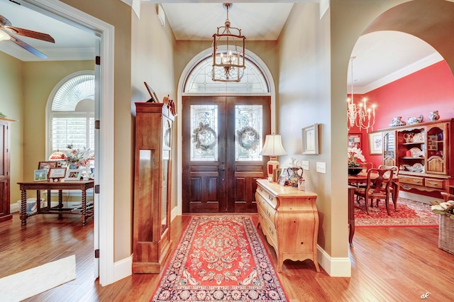 foyer entrance with french doors, light hardwood / wood-style floors, ceiling fan with notable chandelier, and ornamental molding