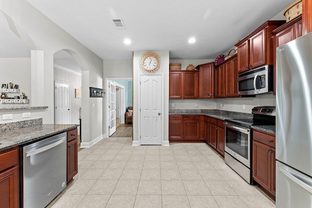 kitchen featuring light tile patterned flooring, stainless steel appliances, and dark stone countertops