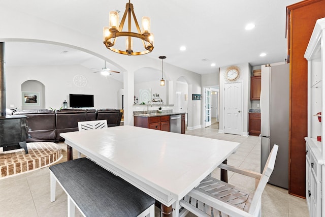 dining area with ceiling fan with notable chandelier, sink, light tile patterned floors, and vaulted ceiling