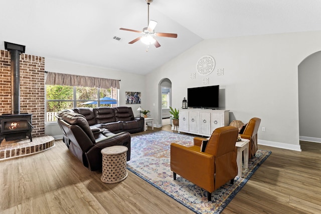 living room with hardwood / wood-style flooring, ceiling fan, a wood stove, and high vaulted ceiling