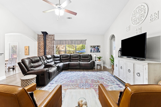 living room featuring light wood-type flooring, high vaulted ceiling, a wood stove, and ceiling fan