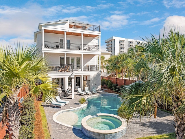 rear view of house with a swimming pool with hot tub, a patio, and a balcony