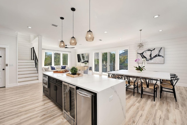 kitchen featuring stainless steel microwave, a center island, hanging light fixtures, wine cooler, and light wood-type flooring