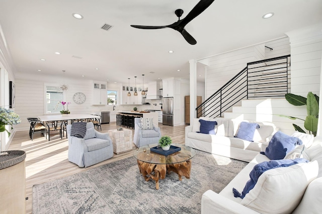 living room with ceiling fan, sink, wood walls, light hardwood / wood-style floors, and ornamental molding