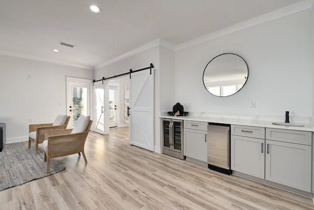 bar with a barn door, light hardwood / wood-style floors, crown molding, and beverage cooler