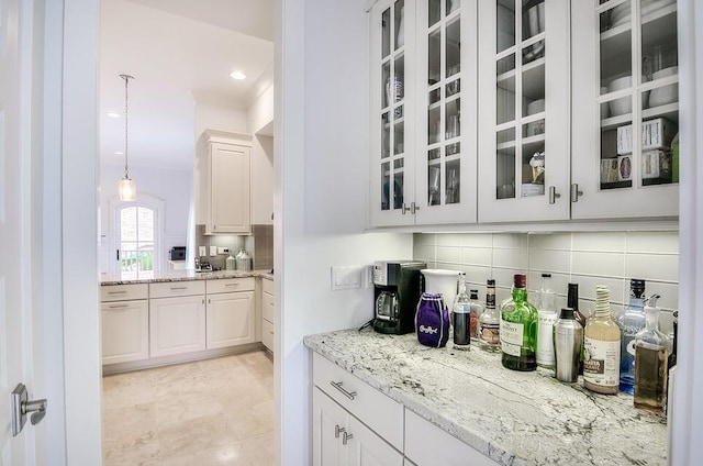 bar with decorative light fixtures, light stone counters, white cabinetry, and decorative backsplash