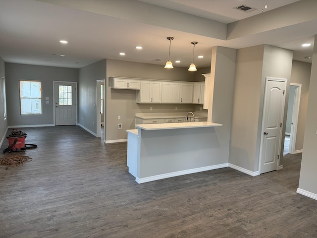 kitchen with a peninsula, dark wood-type flooring, visible vents, baseboards, and white cabinetry