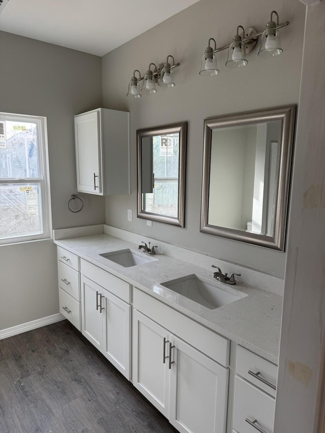 full bath with double vanity, a sink, baseboards, and wood finished floors