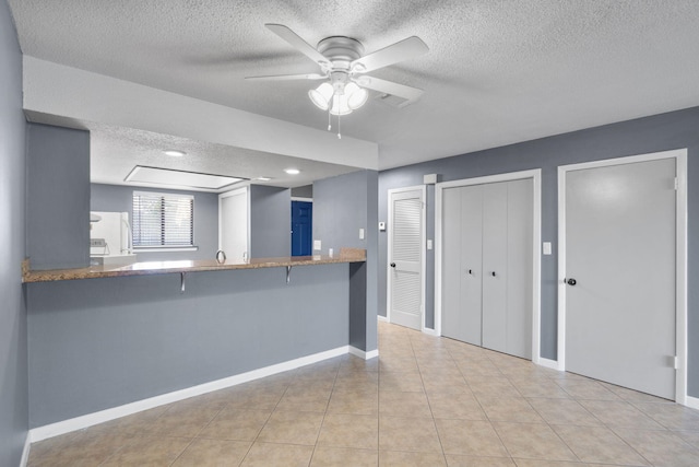 kitchen with a breakfast bar, kitchen peninsula, a textured ceiling, and light tile patterned floors