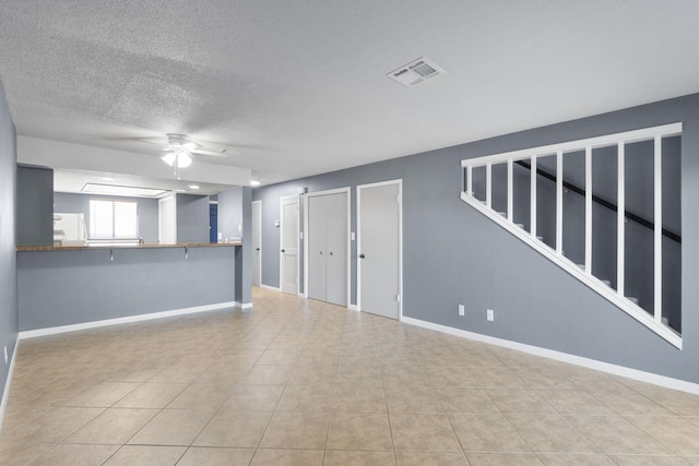 unfurnished living room with ceiling fan, light tile patterned flooring, and a textured ceiling