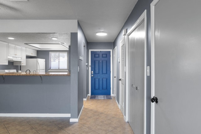 interior space with kitchen peninsula, a textured ceiling, light tile patterned floors, white cabinets, and white fridge