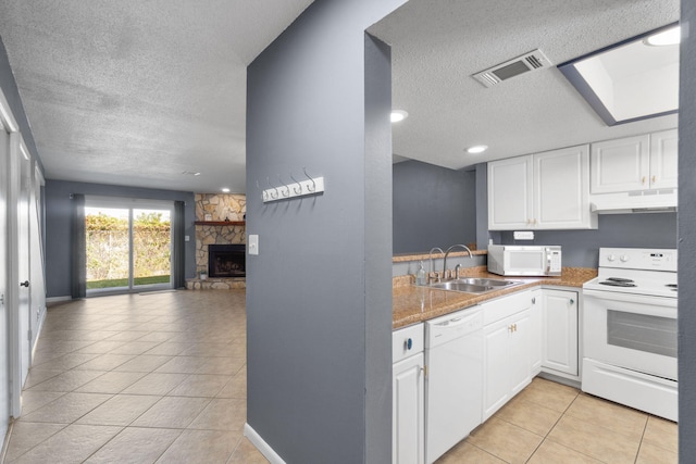 kitchen featuring white appliances, a stone fireplace, light tile patterned floors, a textured ceiling, and white cabinetry