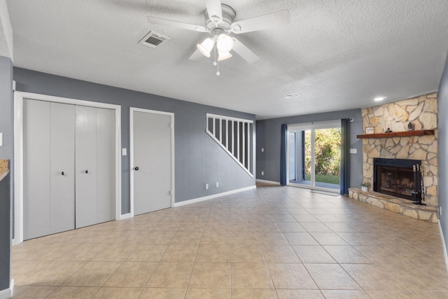 unfurnished living room featuring ceiling fan, a fireplace, light tile patterned floors, and a textured ceiling