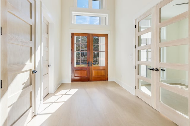 doorway to outside featuring french doors, a towering ceiling, and light wood-type flooring