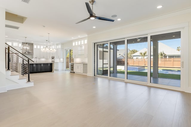 unfurnished living room with crown molding, ceiling fan with notable chandelier, a wealth of natural light, and wine cooler