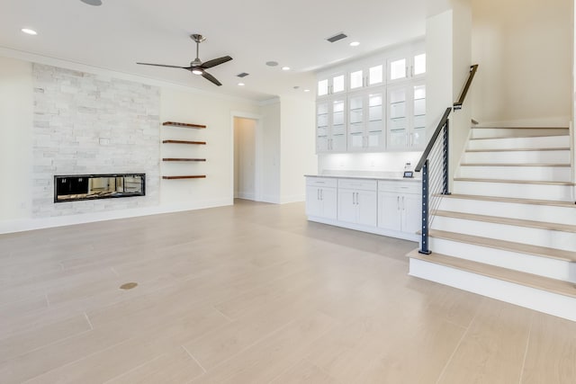 unfurnished living room with ornamental molding, a stone fireplace, and ceiling fan