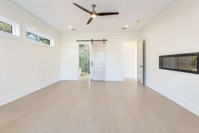 empty room featuring crown molding, ceiling fan, a barn door, and light wood-type flooring