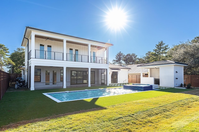 rear view of property featuring french doors, a balcony, a yard, and a pool with hot tub