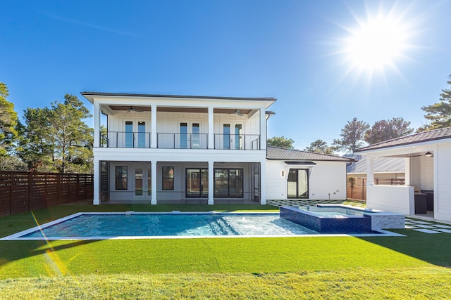 rear view of house featuring ceiling fan, a balcony, a yard, and a pool with hot tub