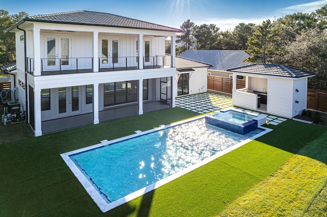 back of house featuring a patio, a balcony, a yard, a pool with hot tub, and french doors