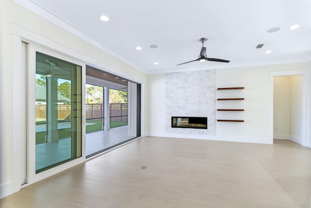 unfurnished living room featuring crown molding, ceiling fan, and a stone fireplace