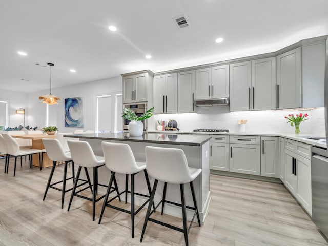 kitchen with light hardwood / wood-style floors, appliances with stainless steel finishes, a breakfast bar area, hanging light fixtures, and gray cabinets