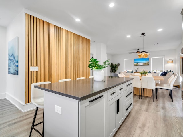 kitchen featuring light hardwood / wood-style floors, a kitchen bar, ceiling fan, a kitchen island, and white cabinets