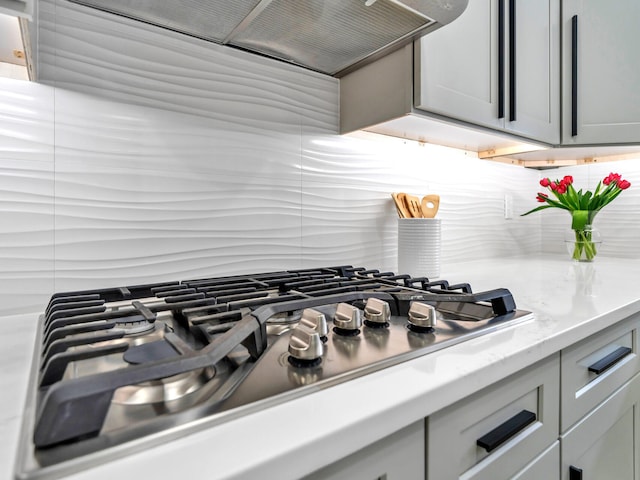 interior details featuring stainless steel gas cooktop, gray cabinets, backsplash, and custom range hood