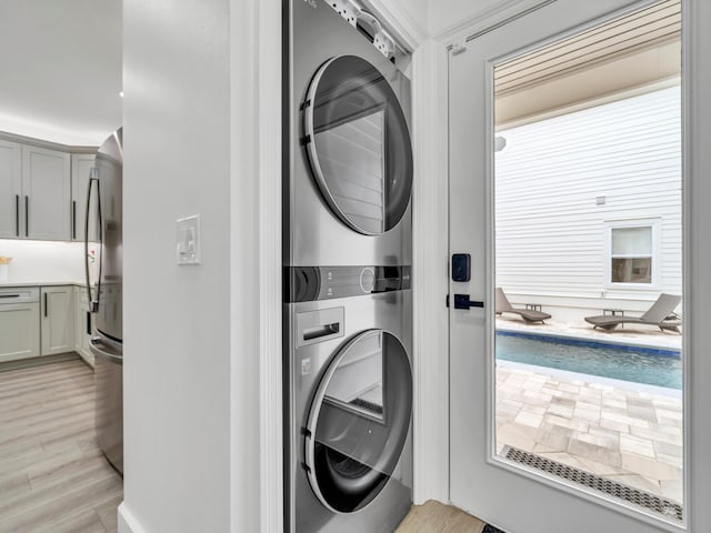 washroom featuring a wealth of natural light, stacked washer and clothes dryer, and light hardwood / wood-style flooring