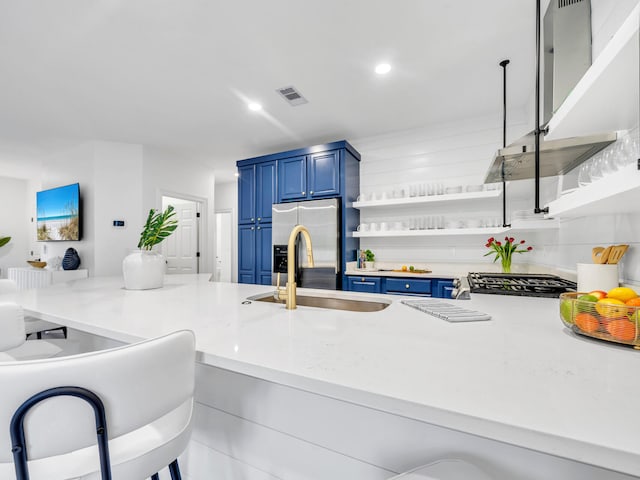 kitchen with sink, a breakfast bar, appliances with stainless steel finishes, range hood, and blue cabinets