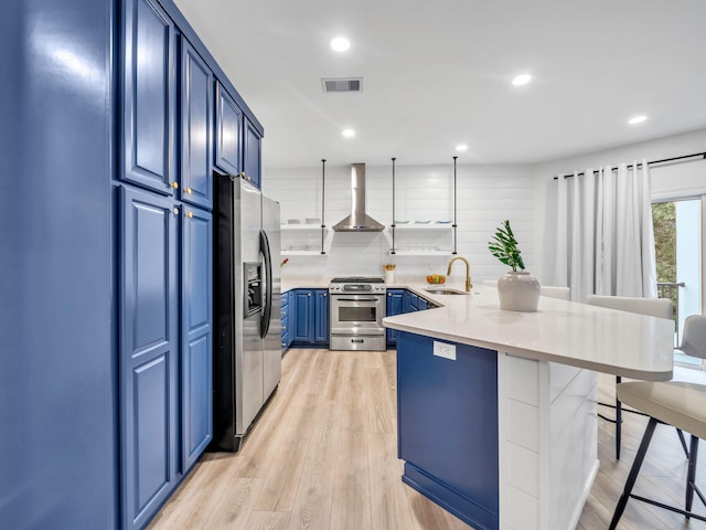 kitchen featuring wall chimney range hood, appliances with stainless steel finishes, blue cabinetry, sink, and a breakfast bar area