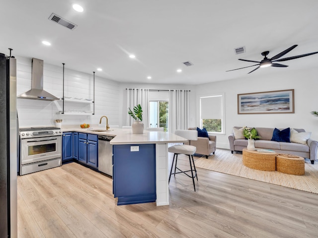 kitchen featuring light hardwood / wood-style floors, kitchen peninsula, appliances with stainless steel finishes, a breakfast bar area, and wall chimney range hood