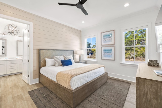 bedroom with ornamental molding, light wood-type flooring, ceiling fan with notable chandelier, and connected bathroom