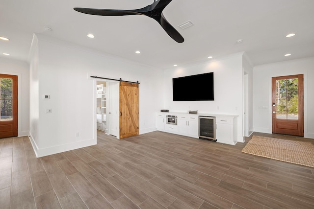 unfurnished living room with crown molding, light hardwood / wood-style floors, a barn door, and beverage cooler