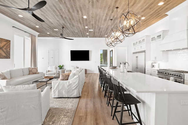 living room featuring light hardwood / wood-style floors, ceiling fan with notable chandelier, wood ceiling, and sink