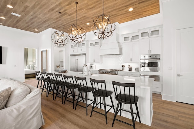 kitchen with appliances with stainless steel finishes, pendant lighting, hardwood / wood-style flooring, wooden ceiling, and a kitchen island with sink