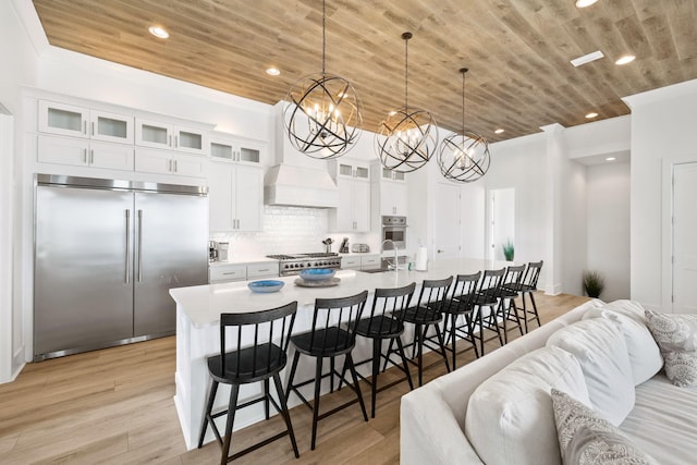 kitchen featuring light wood-type flooring, premium appliances, white cabinetry, and decorative light fixtures