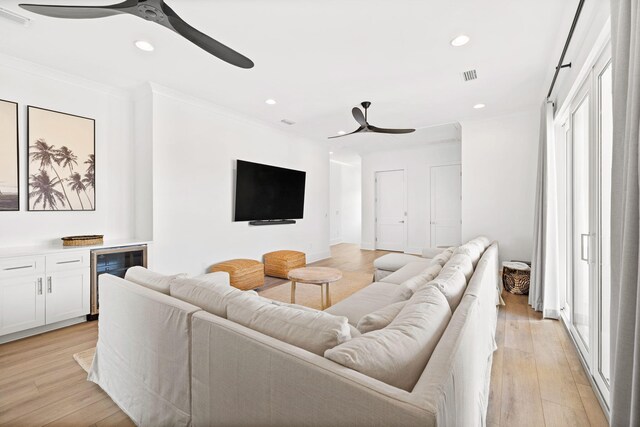 living room with plenty of natural light, wine cooler, light wood-type flooring, and crown molding