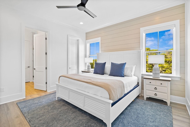 bedroom featuring ceiling fan, wooden walls, light hardwood / wood-style flooring, and ornamental molding