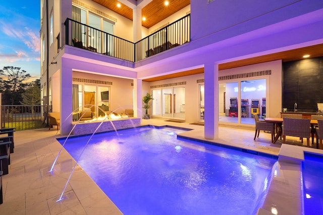 pool at dusk featuring a patio and pool water feature