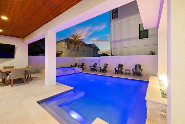 pool at dusk featuring a patio and an in ground hot tub