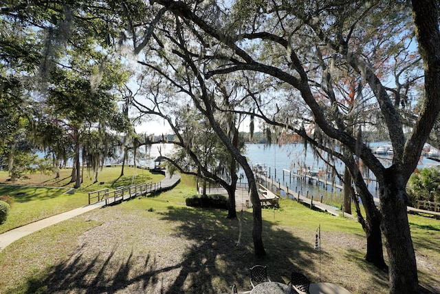 surrounding community featuring a water view, a dock, and a lawn