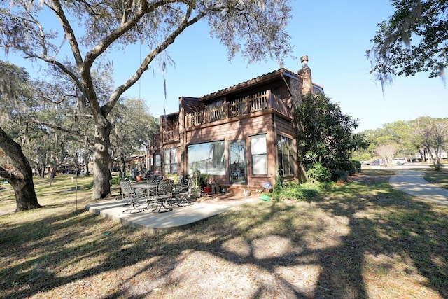 rear view of property featuring a balcony, a yard, and a patio area