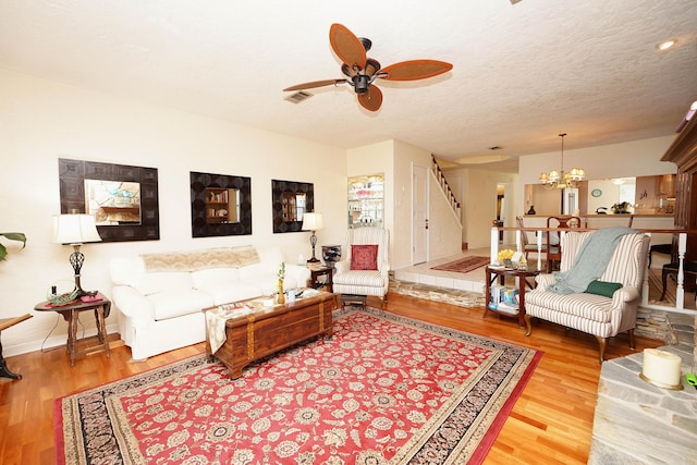 living room featuring ceiling fan with notable chandelier, hardwood / wood-style floors, and a textured ceiling