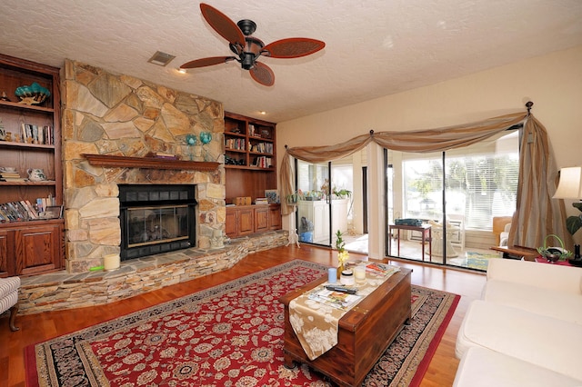 living room with ceiling fan, a stone fireplace, a textured ceiling, and light hardwood / wood-style floors